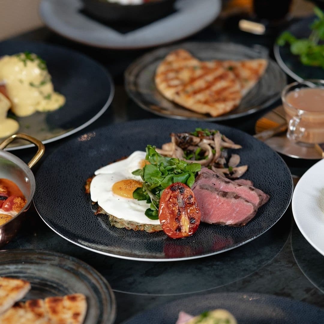 Gourmet breakfast plate with fried egg, roasted tomato, sliced steak, and greens at The Cut & Craft.