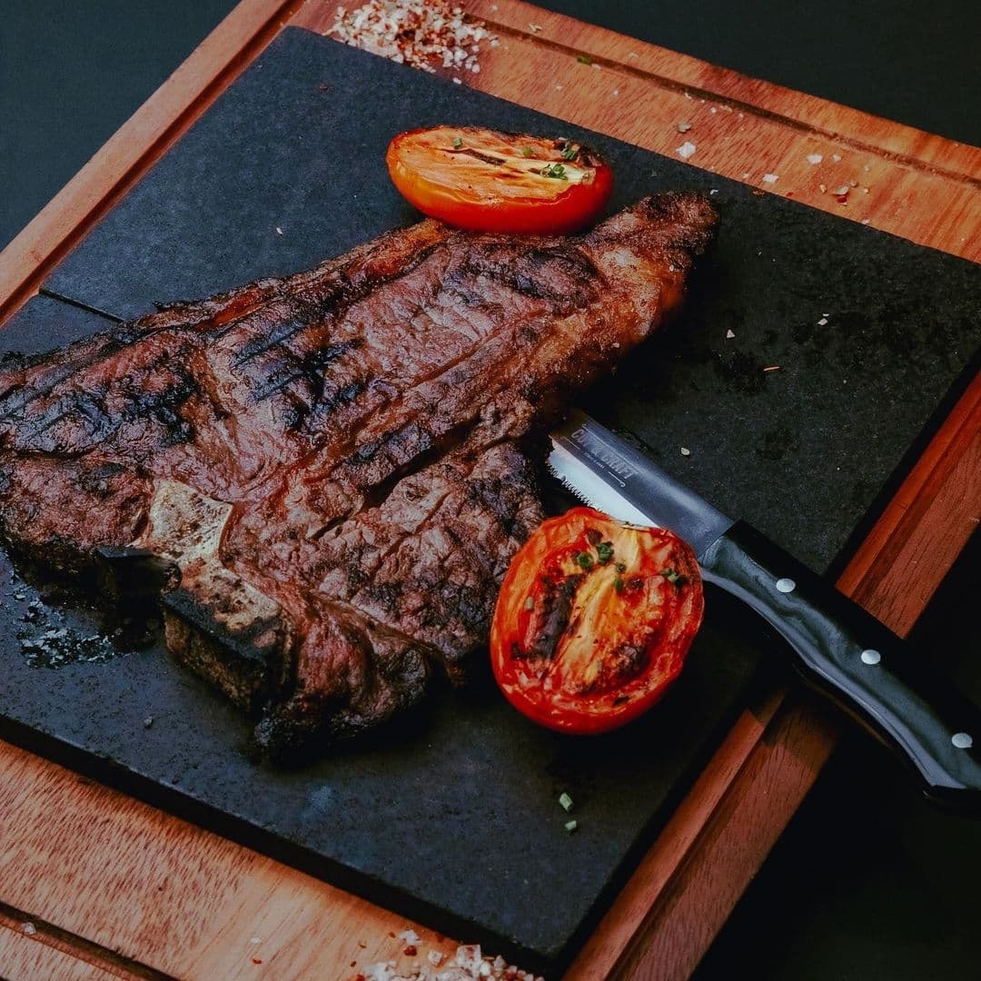 Grilled T-bone steak served on a slate board with roasted tomato at The Cut & Craft.