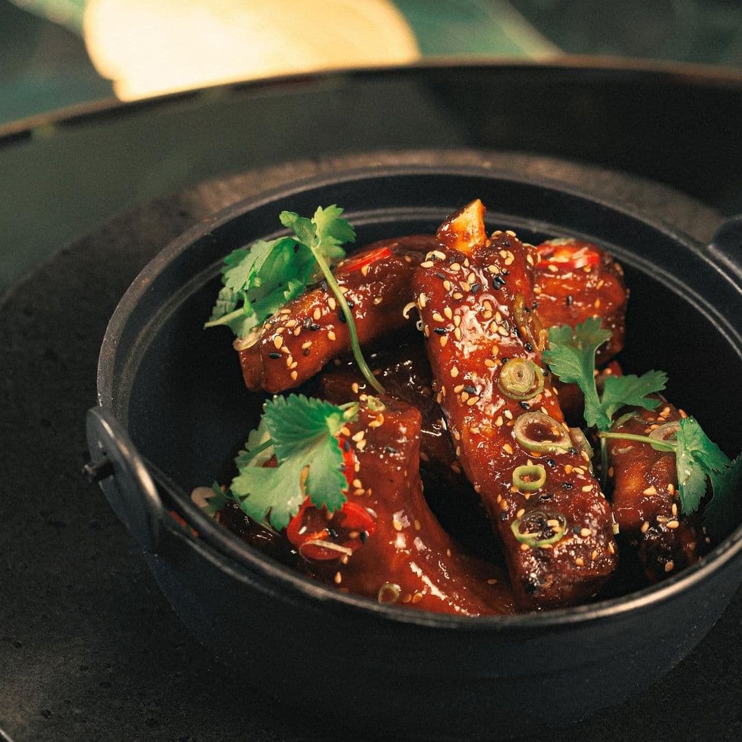 Delicious glazed ribs garnished with sesame seeds and fresh cilantro served at The Ivy Asia.