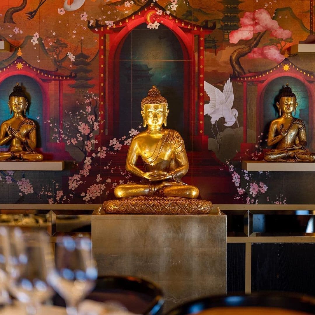 Interior of The Ivy Asia featuring golden Buddha statues, traditional Asian artwork with cherry blossoms, and elegant table settings.