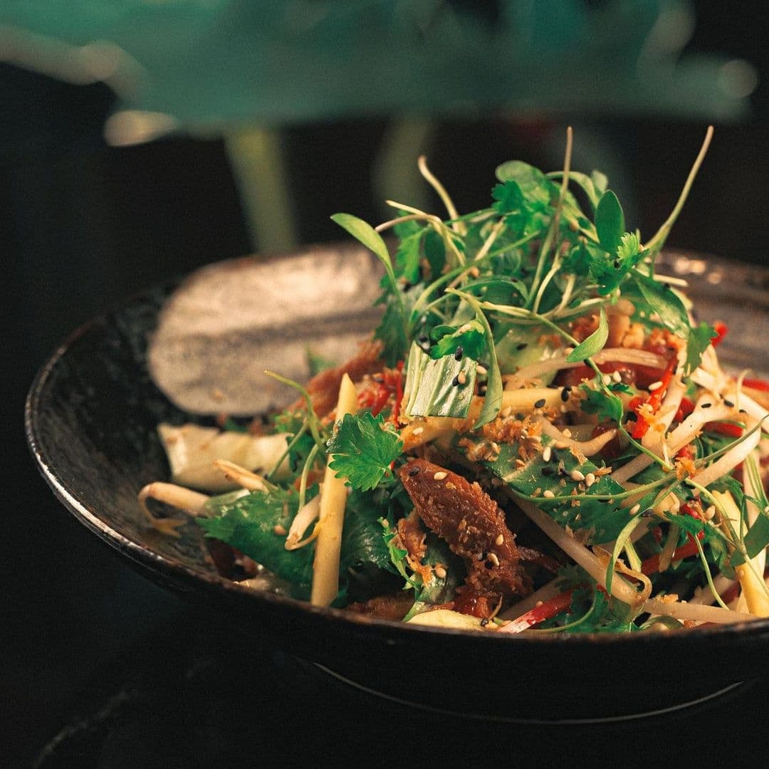 Fresh Asian-style salad served at The Ivy Asia, featuring mixed greens, herbs, nuts, and crispy elements in a dark bowl.