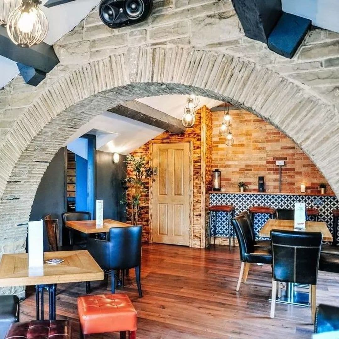 Interior of The Malt Brewhouse featuring stone archways, wooden tables, leather chairs, and exposed brick walls with decorative lighting.