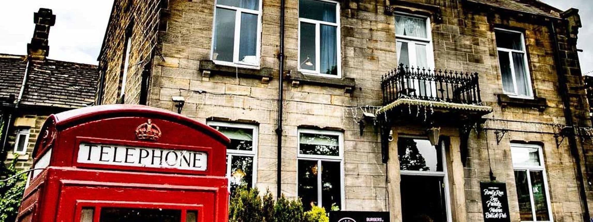 Exterior view of The Old Kings Arms, featuring a classic red British telephone box in the foreground with the stone facade of the pub behind it, adorned with windows and a balcony with iron railings.