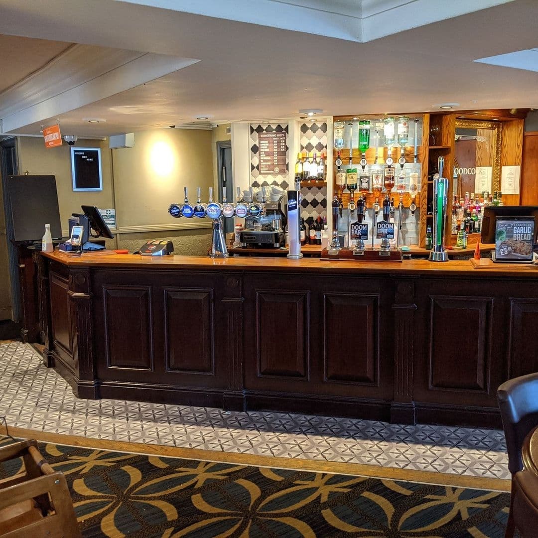 Interior view of The Woodcock New Farnley bar with a selection of draught beers, spirits on shelves, and a patterned floor.