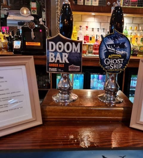 Beer taps featuring Doom Bar Amber Ale and Adnams Ghost Ship Citrus Pale Ale at The Merchant pub bar with a selection of spirits in the background.