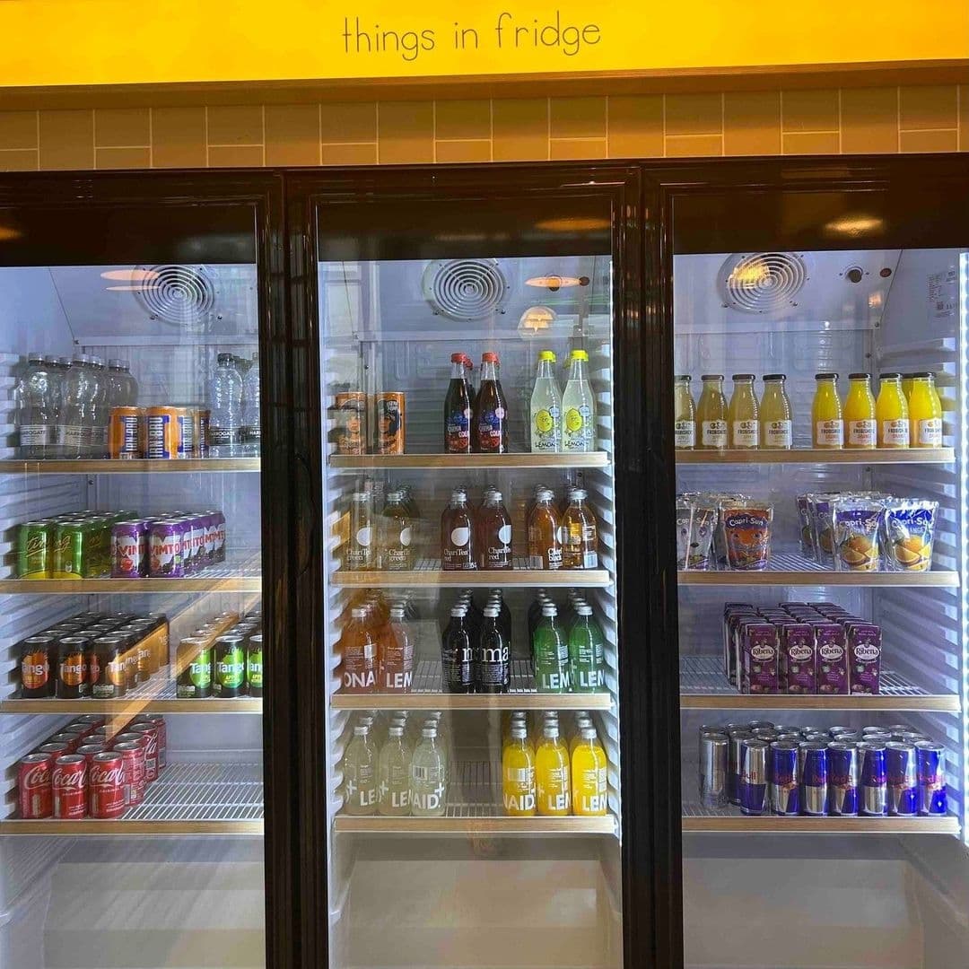 Refrigerated display at Things in Bread featuring an assortment of beverages, including sodas, juices, and water, neatly arranged on shelves.