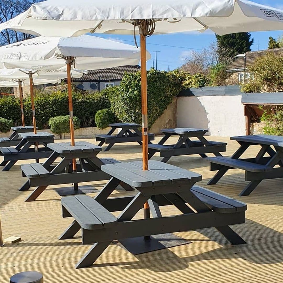 Sunny outdoor seating area with wooden picnic benches under white umbrellas at Three Horse Shoes Oulton.
