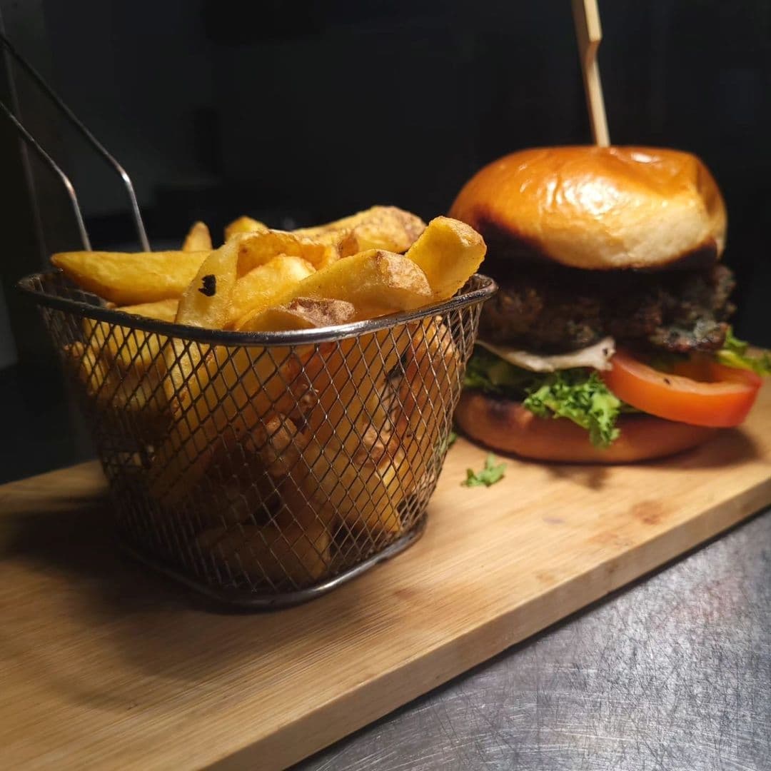 Gourmet burger with lettuce and tomato on a brioche bun, served with a side of golden fries in a metal basket, at Three Horse Shoes Oulton.