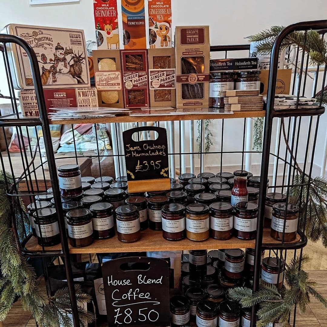 Shelves stocked with an assortment of gourmet products including jams, chutneys, marmalades, and coffee at Truly Scrummy, with price tags visible.
