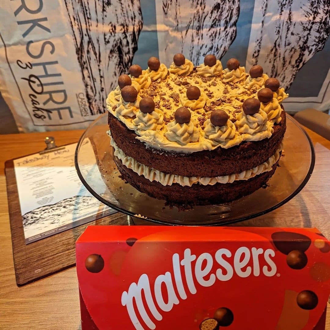 A decadent layered chocolate cake topped with cream and Maltesers on display at Truly Scrummy.