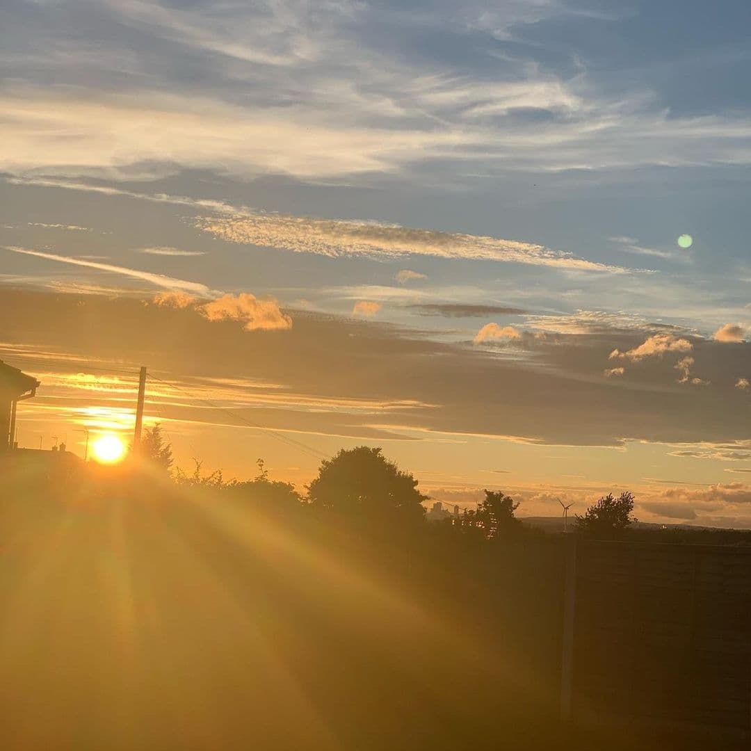 Sunset at Two Pointers with golden sunlight piercing through scattered clouds in a blue sky, casting rays over the silhouette of a landscape.