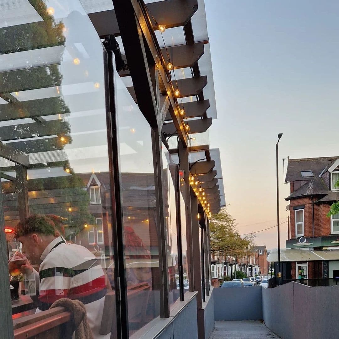 Exterior view of Victoria Social with string lights along the facade, reflecting the warm ambiance inside where patrons are dining, at dusk.
