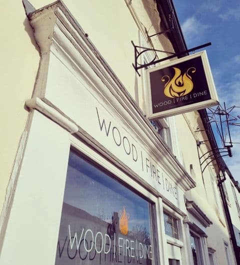 Exterior view of WOOD FIRE | DINE Pizzeria with signage above the window on a sunny day.