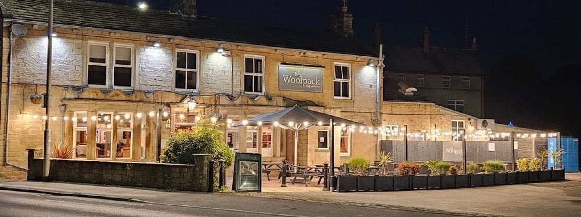Exterior night view of Woolpack Inn with illuminated facade, outdoor seating area, and string lights.