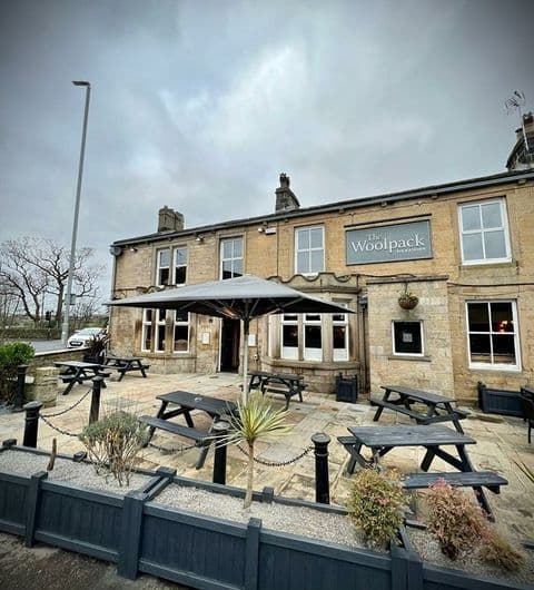 Exterior view of Woolpack Inn with outdoor seating and a large umbrella, set against a cloudy sky.