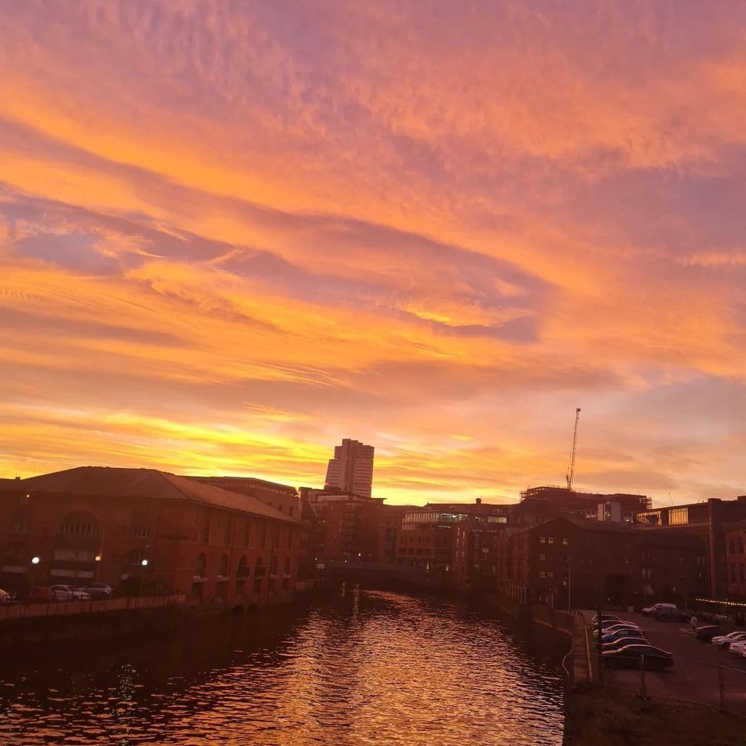 Sunset view over the river near Aire Bar with orange and pink clouds in the sky reflecting on the water, surrounded by buildings.