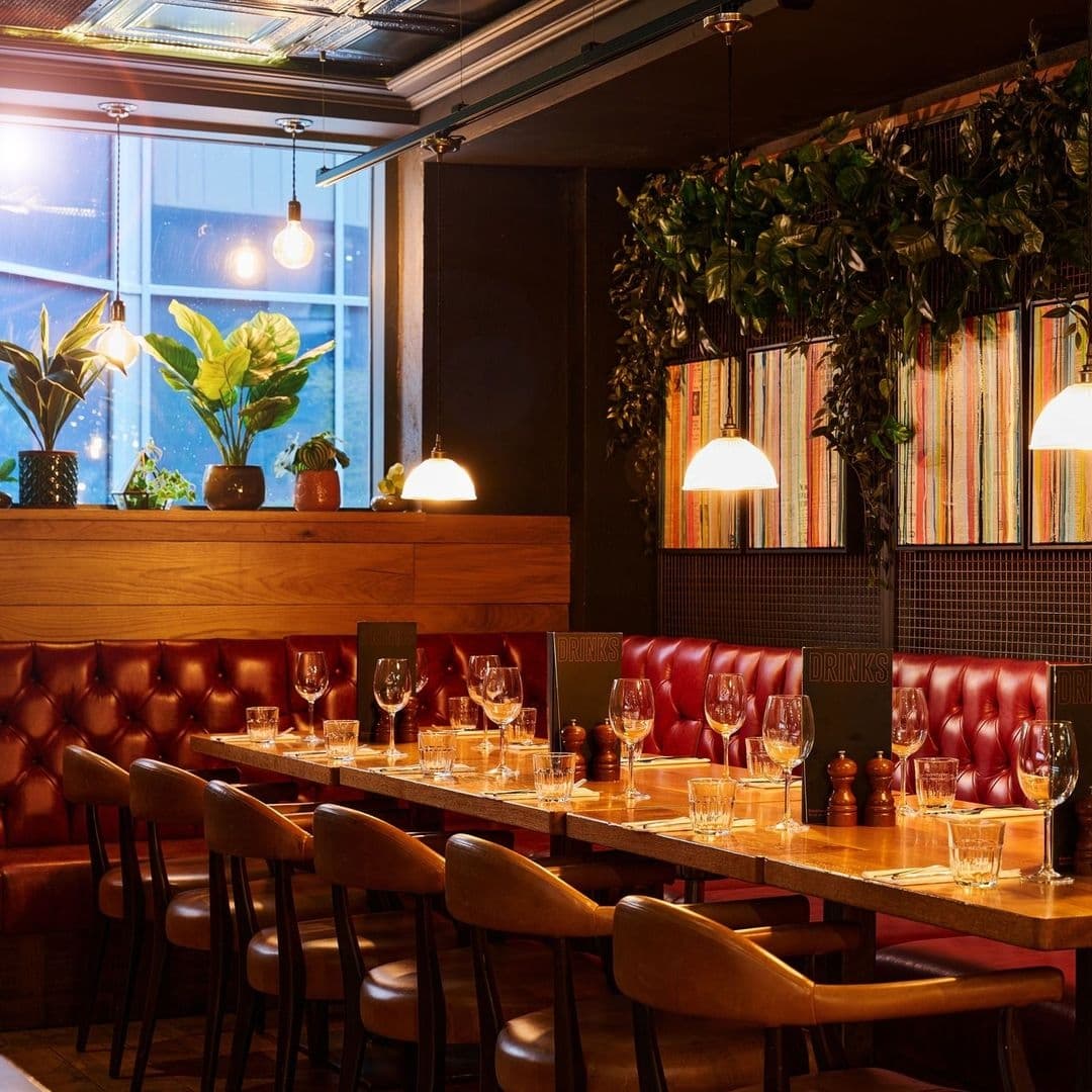 Cozy dining area at Blackhouse with red leather booths, wooden tables set with glassware, and a bookshelf lined with colorful books under warm lighting.