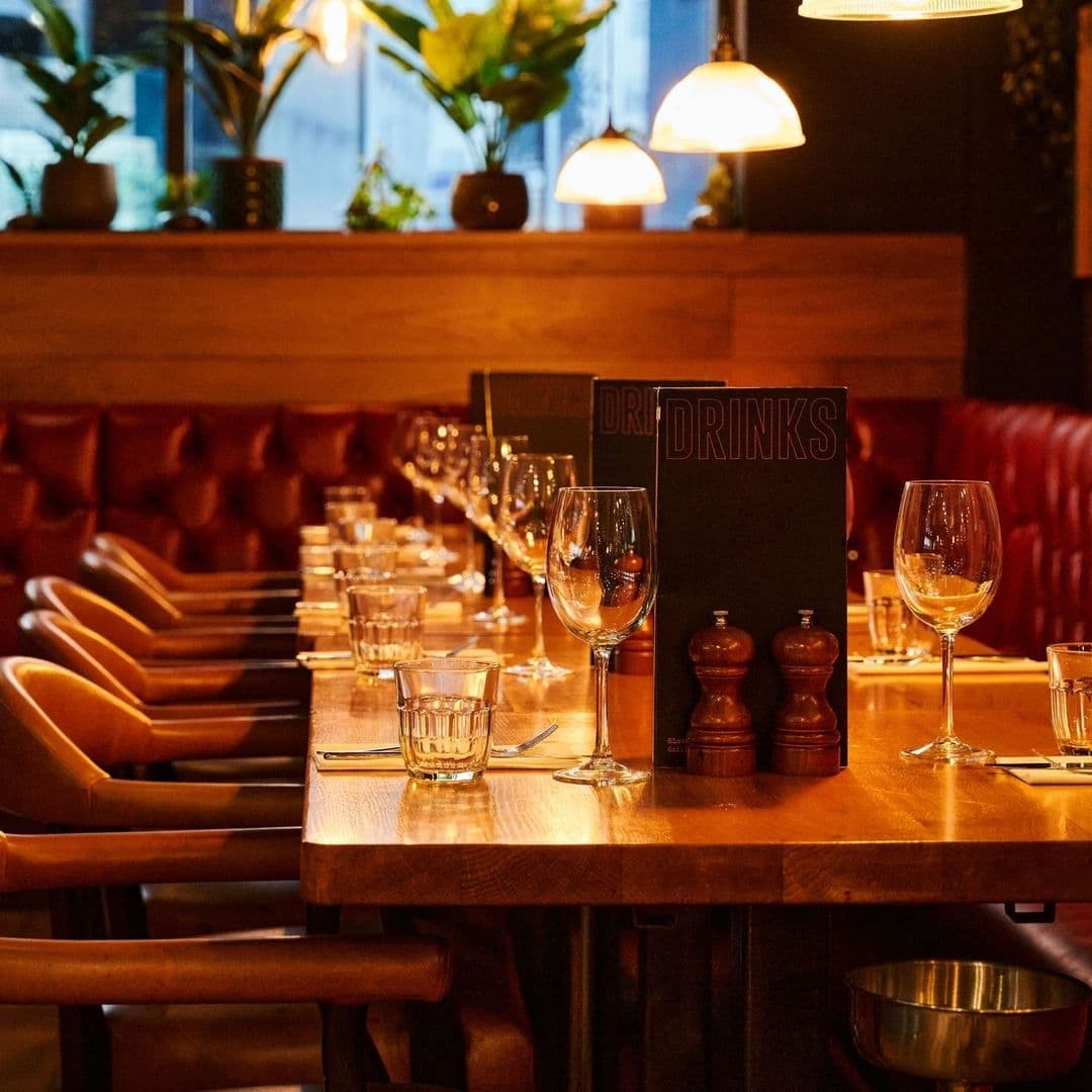 Cozy dining setup at Blackhouse with wine glasses on a wooden table, warm lighting, and comfortable seating.