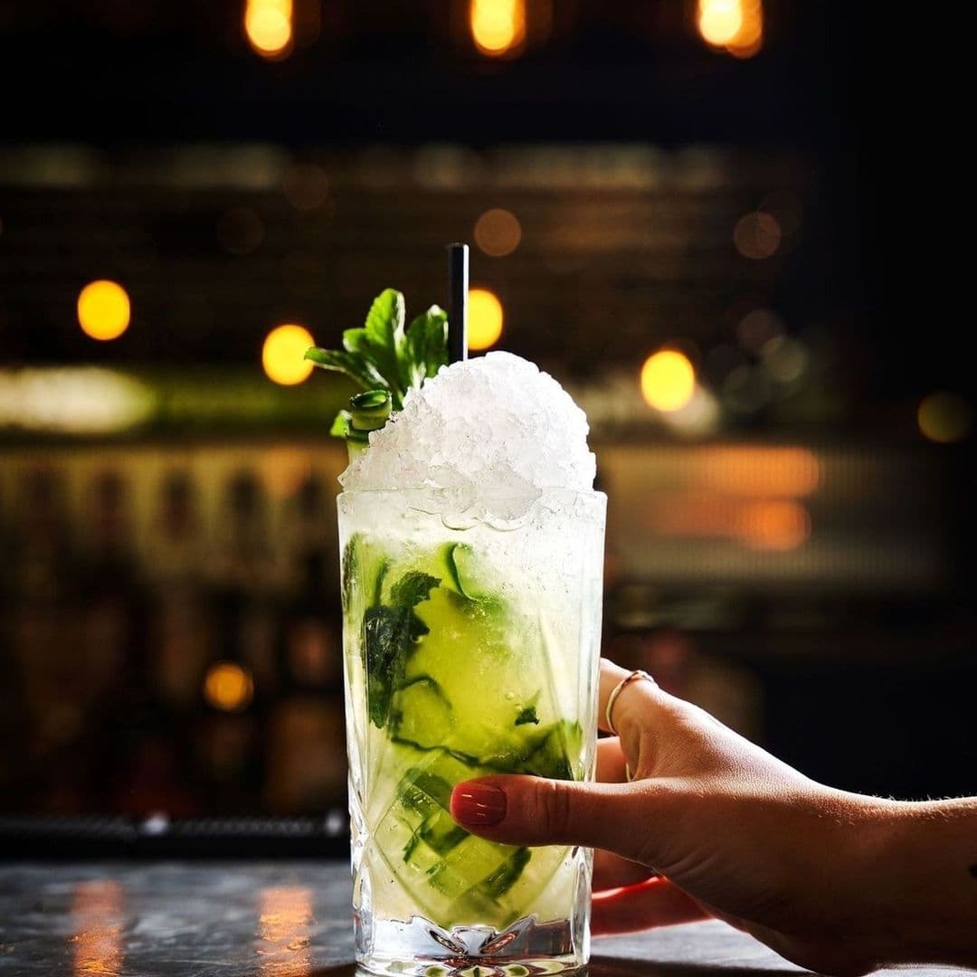 A hand holding a mojito cocktail with fresh mint and crushed ice at Blackhouse.