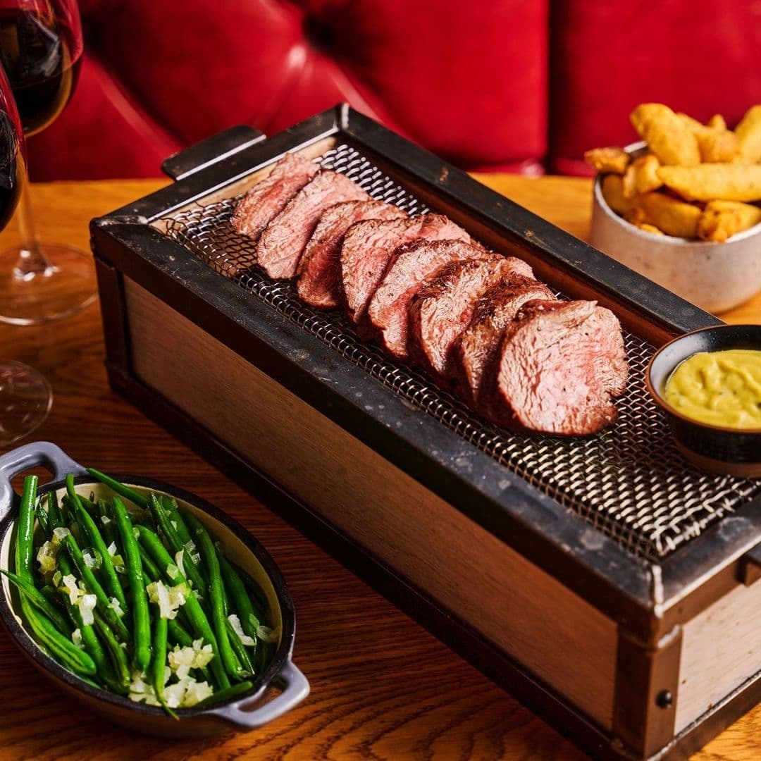 Sliced steak served on a metal grill over a wooden box, with a side of green beans and potato wedges, at Blackhouse.