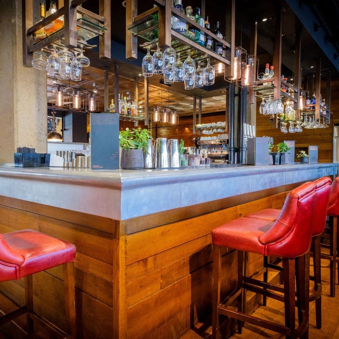 Interior of Blackhouse showing a stylish bar with red leather stools, hanging glassware, and a selection of drinks on shelves.