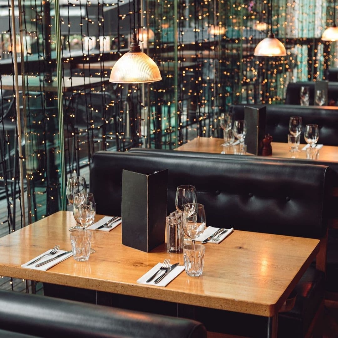 Elegant dining setup at Blackhouse with a wooden table, leather seating, and sparkling fairy lights in the background.