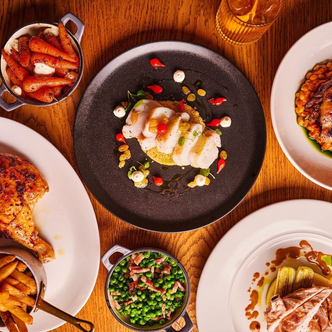 Gourmet dining experience at Blackhouse featuring a variety of dishes, including a plate of scallops, roasted chicken, peas with bacon, and honey-glazed carrots.