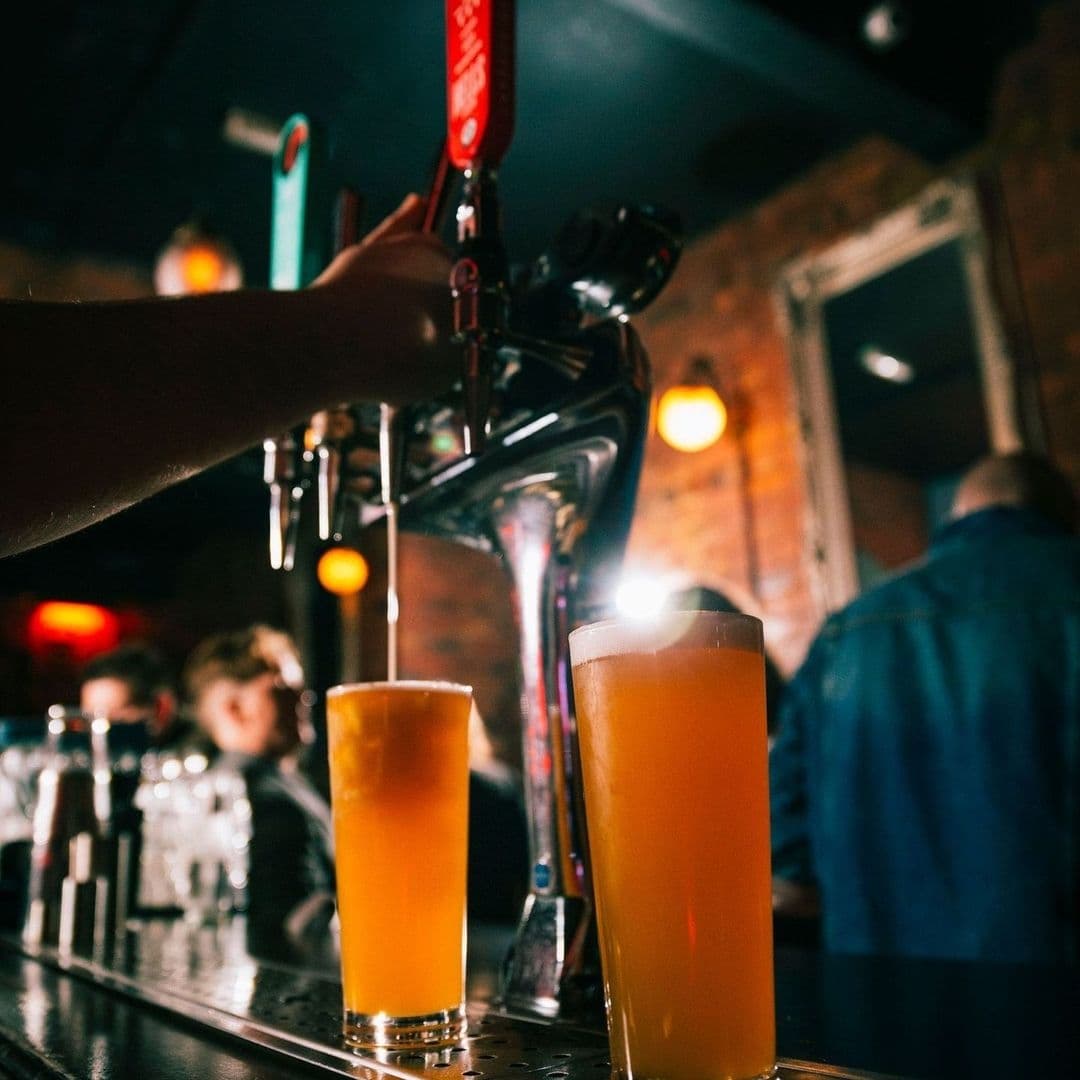 Bartender pouring a craft beer at Call Lane Social with two full pint glasses on the bar and patrons in the background.