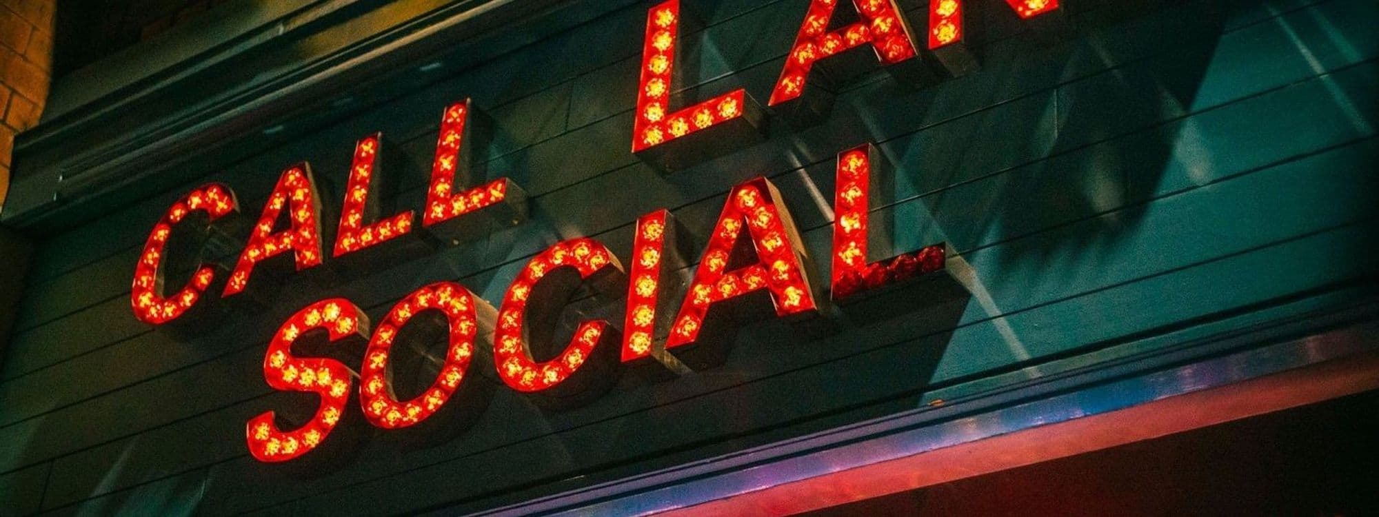 Illuminated red neon sign reading "CALL LANE SOCIAL" on a dark building facade at night.