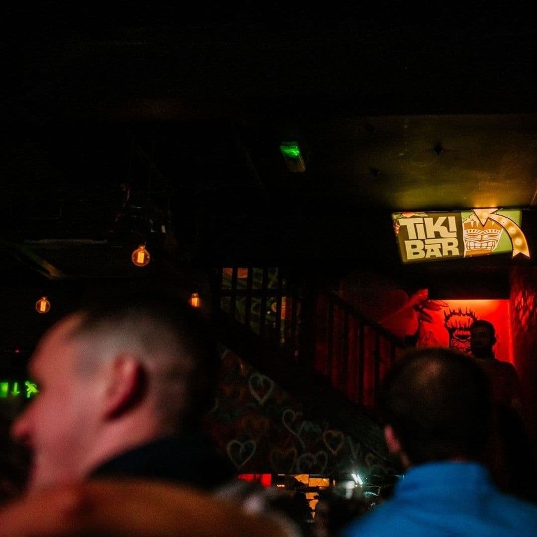 Patrons enjoying a vibrant night out at Call Lane Social with a view of the Tiki Bar sign and warm ambient lighting.