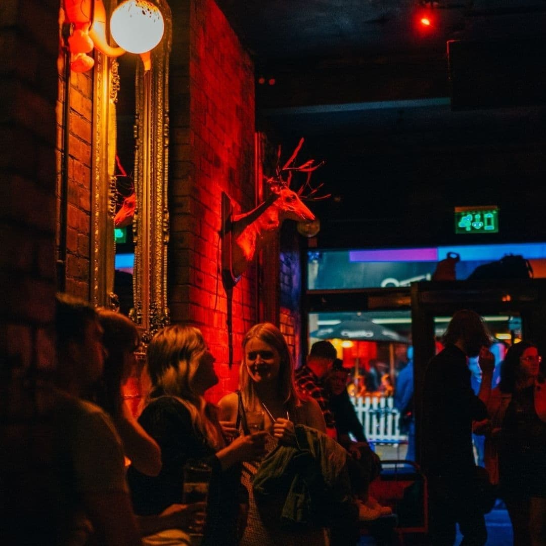 Patrons socializing in the warm, ambient lighting of Call Lane Social, with decorative stag heads mounted on a brick wall.