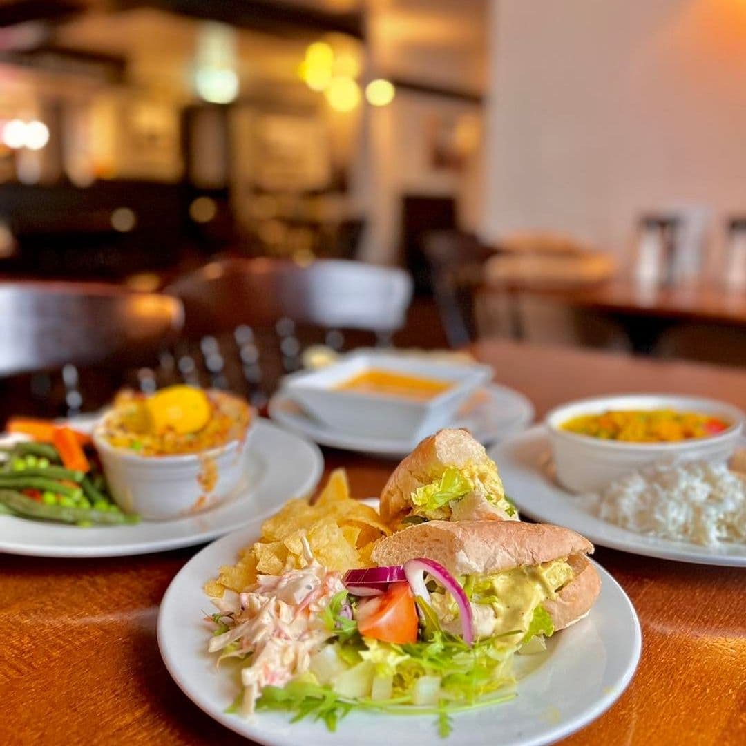 Delicious meal at Fox & Hounds featuring a sandwich with salad and crisps, with bowls of soup and rice dishes in the background, set in a cozy dining atmosphere.