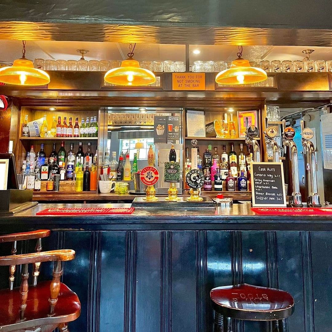 Interior view of the Fox & Hounds bar showcasing a variety of drinks, beer taps, and a well-stocked bar counter under warm pendant lighting.