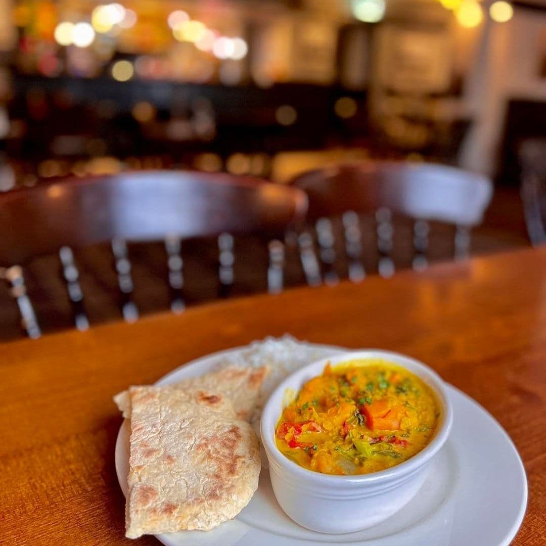 Delicious meal served at Fox & Hounds, featuring a bowl of colorful vegetable curry with fresh flatbread on a wooden table, with the cozy pub ambiance blurred in the background.