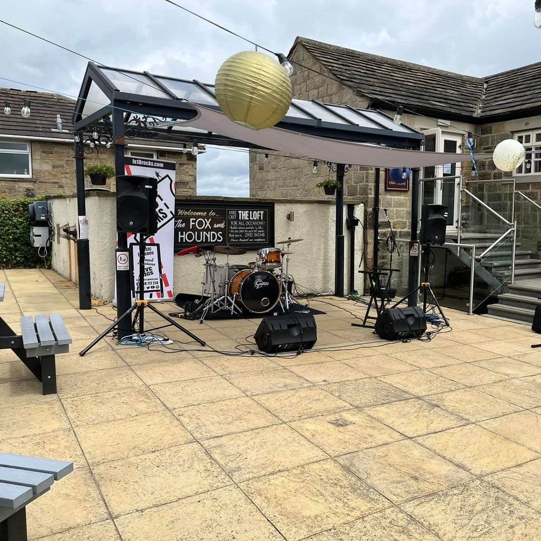 Outdoor music stage setup at Fox & Hounds with drum kit and speakers, ready for a live performance.