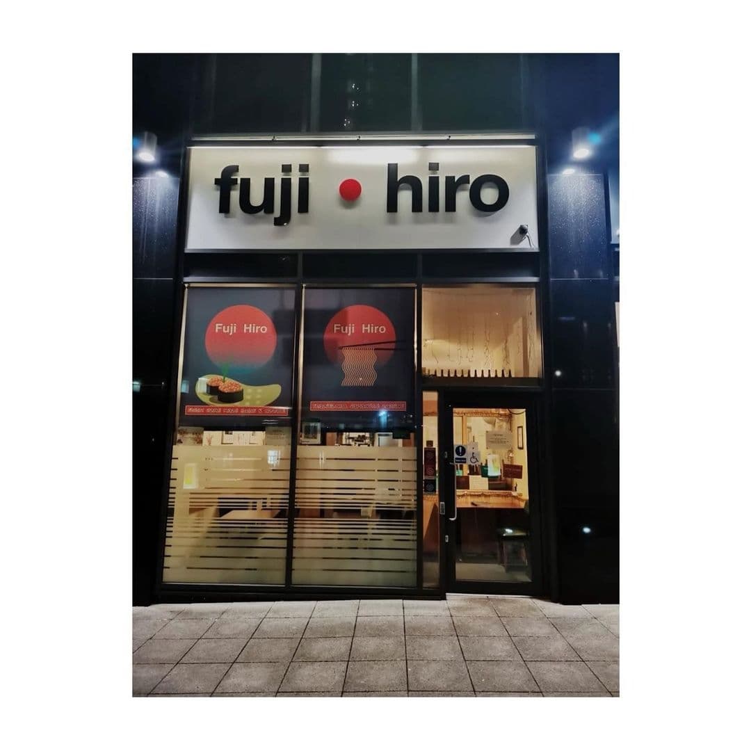 Exterior view of Fuji Hiro restaurant at night with illuminated signage and promotional posters in the windows.