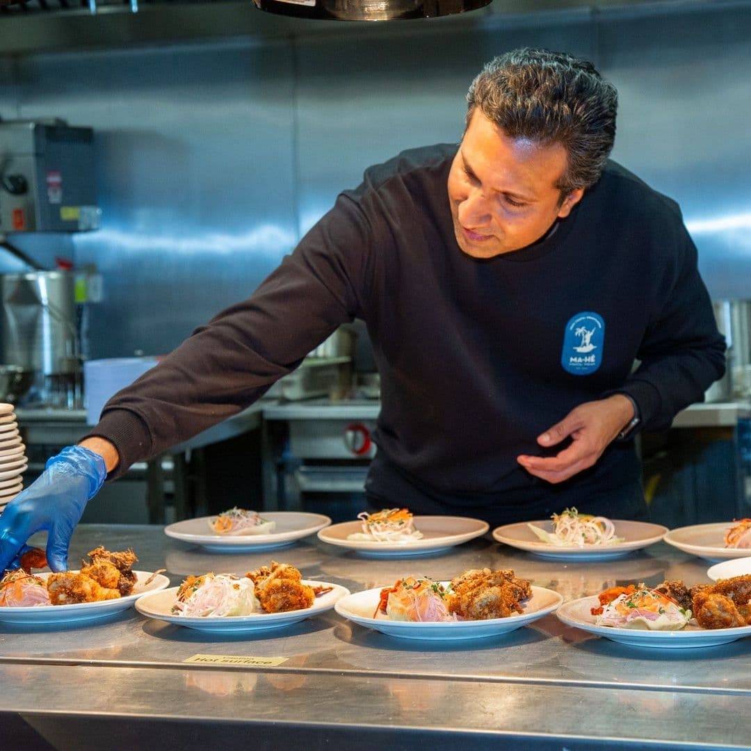 Chef at Ma-Hé Coastal Indian preparing plates of food in a professional kitchen.