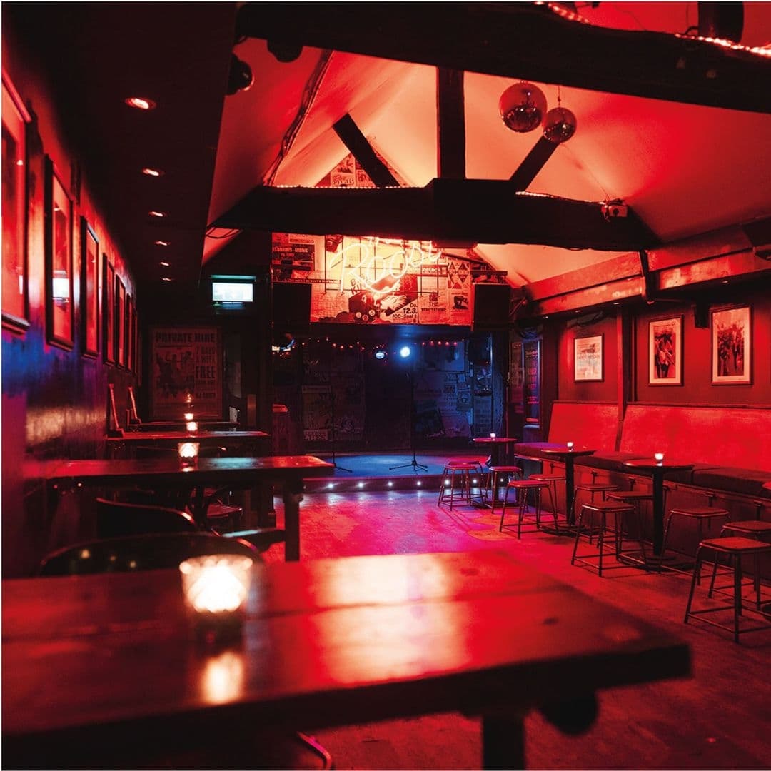 Interior of Smokestack featuring dim red lighting, wooden tables, stage for live performances, and walls adorned with posters and artwork.