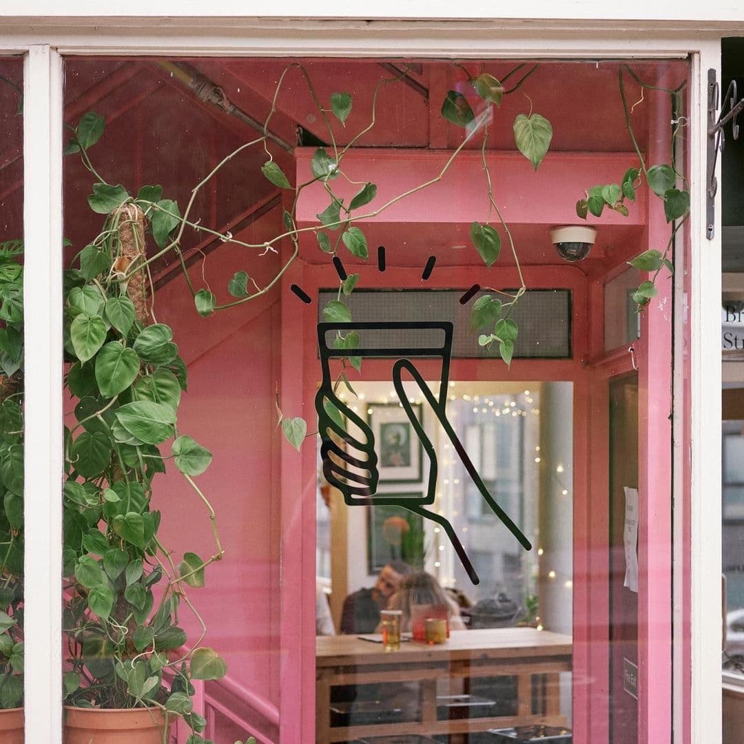 Alt text: "Cozy entrance of The Brunswick adorned with green potted plants and a whimsical drawing of a light bulb on the window, reflecting a warm and inviting interior."