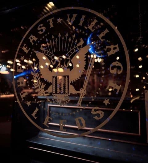Decorative window decal featuring an eagle and stars with the text "The East Village" at a local establishment, illuminated by warm ambient lighting.