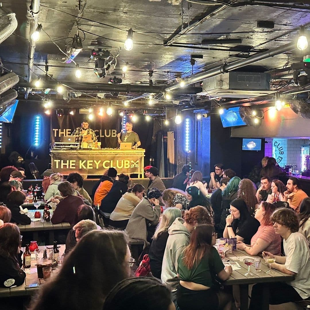 "Lively atmosphere at The Key Club with a crowd enjoying a performance by musicians on stage, surrounded by casual seating and vibrant lighting."