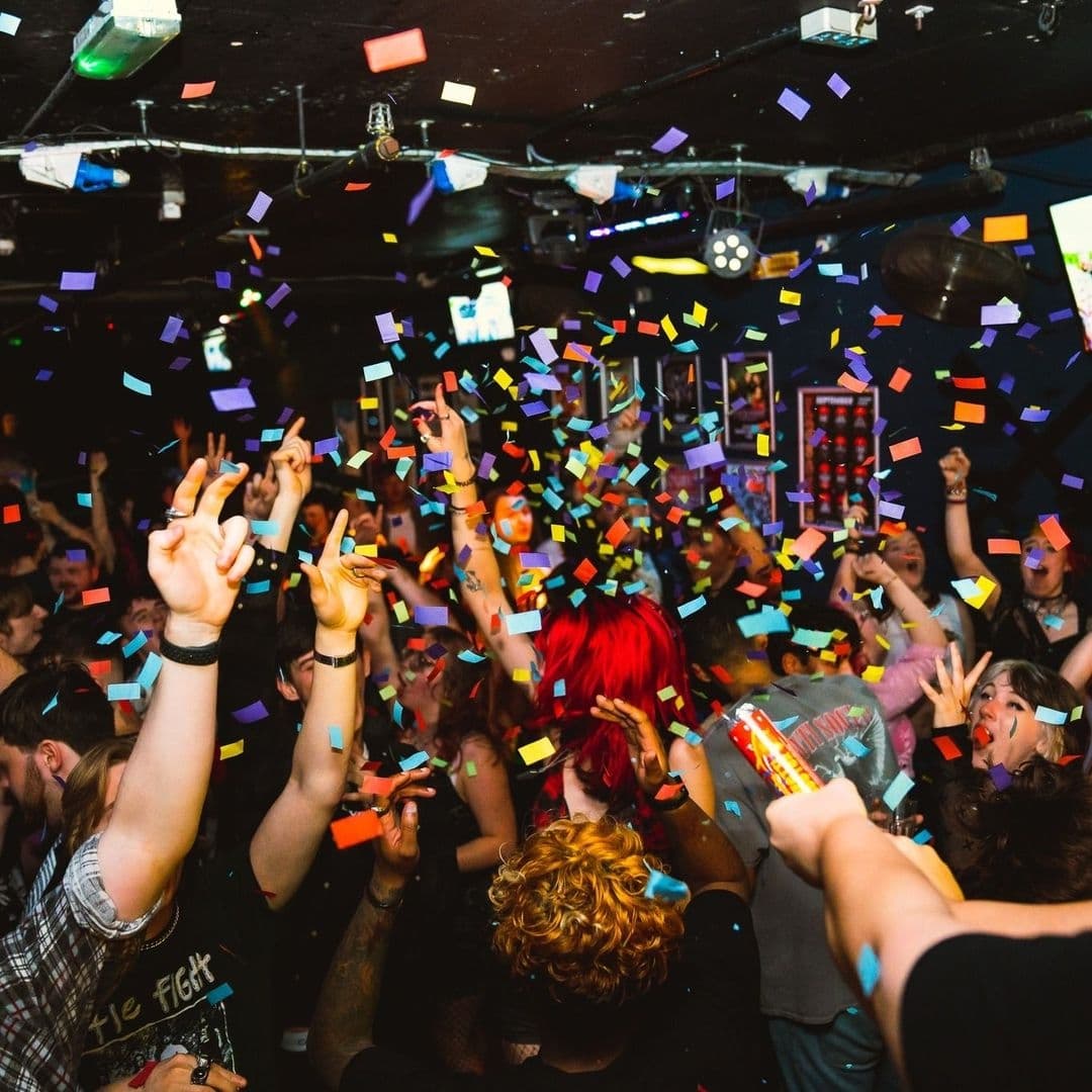 Energetic crowd celebrating with hands up amidst colorful confetti at The Key Club.