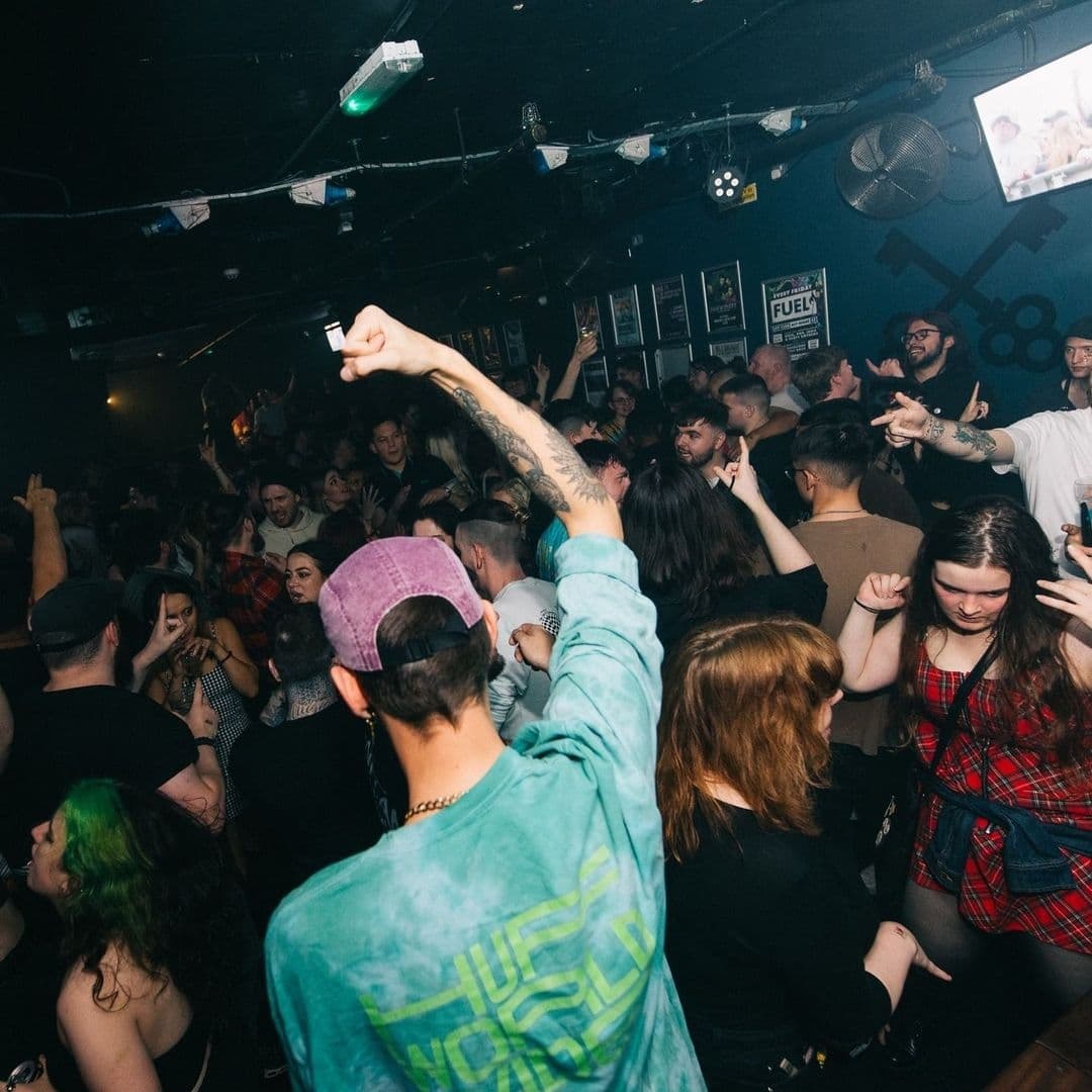Crowd of people enjoying a lively night out at The Key Club, with many individuals dancing and raising their hands in the air, under dim club lighting.