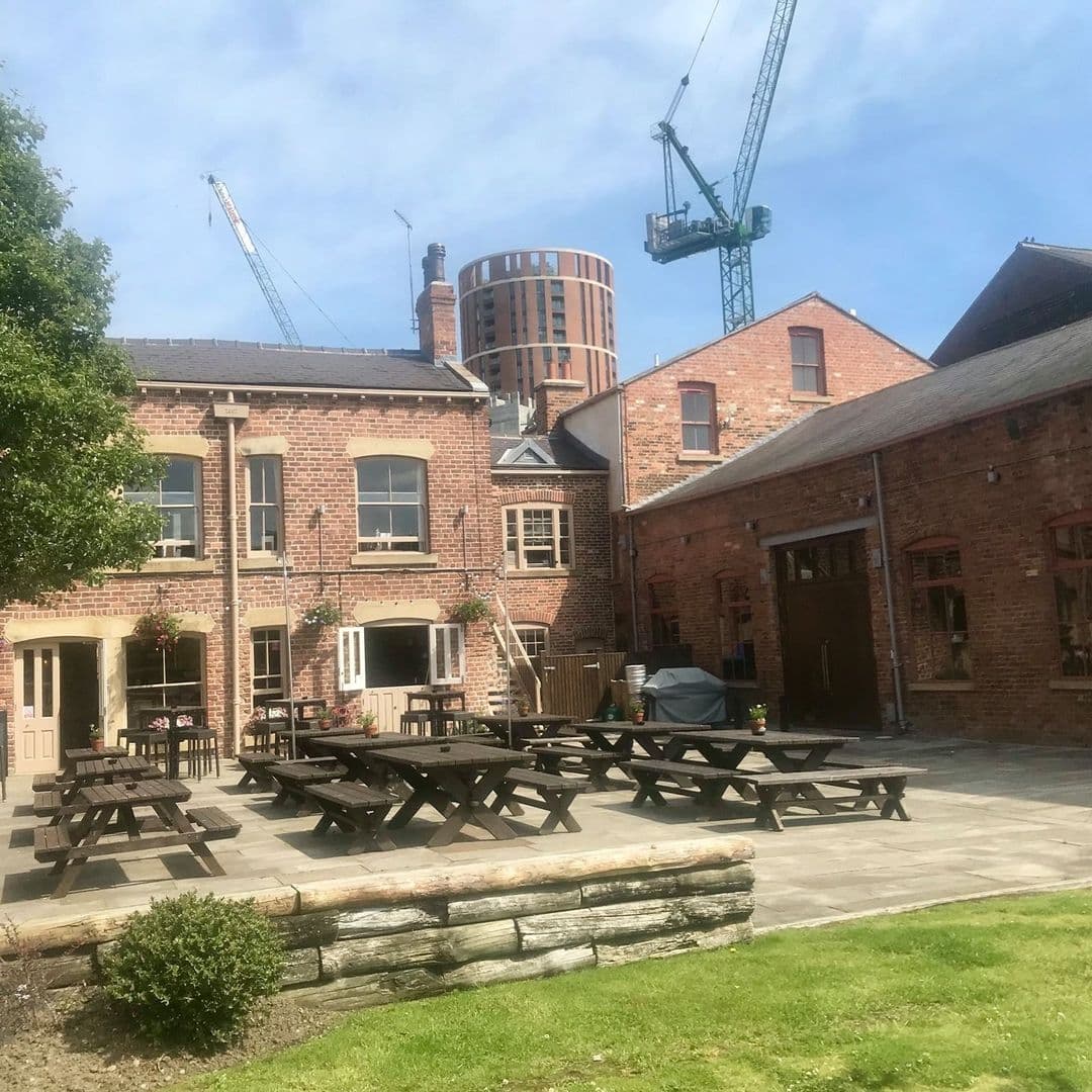 Outdoor seating area with wooden picnic tables at The Midnight Bell, a traditional brick building with clear skies above.