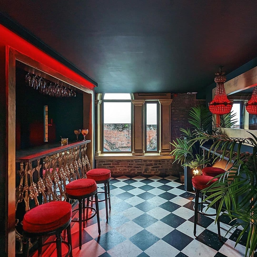 Interior of Viaduct Showbar with a cozy corner featuring a bar with red accent lighting, black and white checkered floor, red bar stools, and large windows providing natural light.
