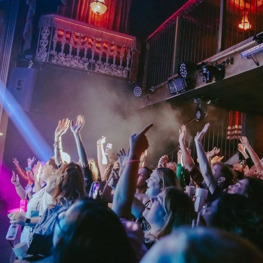 Crowd enjoying a live performance at Viaduct Showbar with hands raised and stage lights illuminating the venue.
