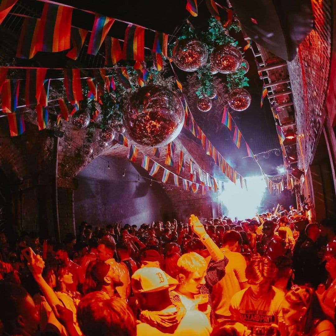 Crowd of people enjoying a vibrant night scene with colorful flags and disco balls at Viaduct Showbar.