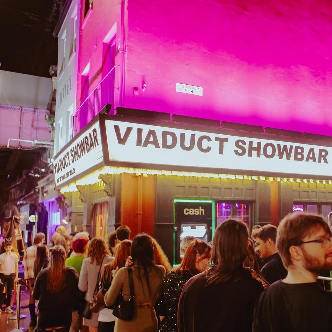 Crowd of people outside Viaduct Showbar at night with vibrant pink lighting.