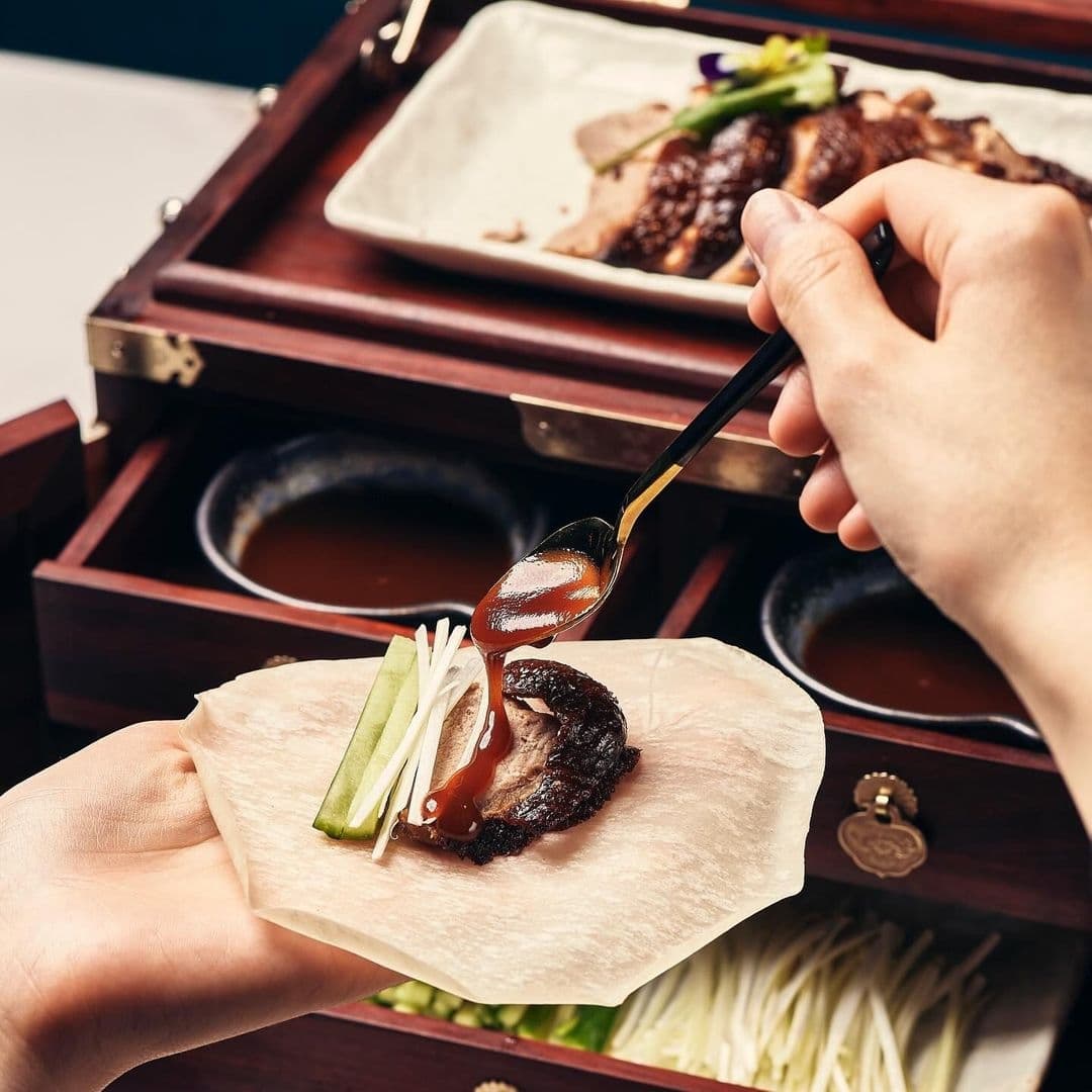 Person preparing a traditional dish with sliced meat, cucumber, and sauce on a flatbread at Blue Pavilion.