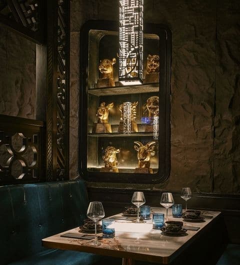 Elegant dining setup at Blue Pavilion featuring a table with glassware and a lit display cabinet with golden decorative items in the background.